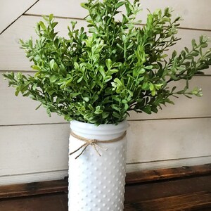 A bouquet of artificial boxwood greenery in a white glass vase.