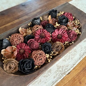 This shows a large coffee table display with a wood dough bowl. The wood is has a dark, moody arrangement of wood flowers and dried botanical berries.