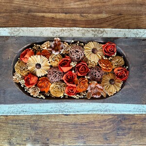 This shows a long wood dough bowl with and arrangement of wood flowers and natural dried botanical berries. The display sits on a coffee table.