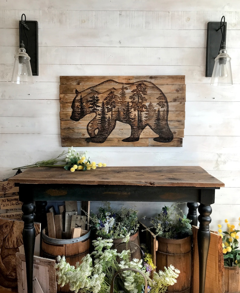 Extra large wall art. Made with reclaimed wood, and features a silhouette of a black bear with a forest scene. Artwork is a wood burning by hand. Wood is a weathered brown. The artwork is dark, burned brown.