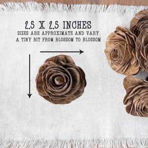 This shows a chocolate brown colored wood flower blossom sitting on a linen cloth. Arrows indicate that it is 2.5 by 2.5 inches.