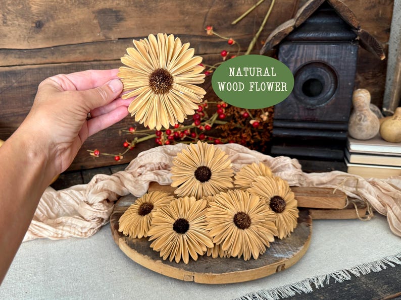 This shows several wood flowers that look like Gerba Daisies. They are laid our on a beige table runner, on top a a vintage style bread board. I am holding one blossom up to show the size and scale of the flower.