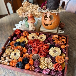 This shows a large wood tray sitting on a dinning room table. The tray is shallow and is holding a large assortments of wood flowers. The flowers are shown in many fall colors such as orange and burgundy. A pumpkin gourd sits in the back.