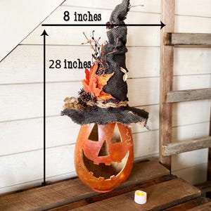 A Large handmade pumpkin witch used for fall decorating. Made from a real dried gourd. The pumpkin, named Hocus Pocus, has a tall burlap crinkled witch hat with a fall leaf arrangement. The gourd measures 28 inches tall and 8 inches wide.