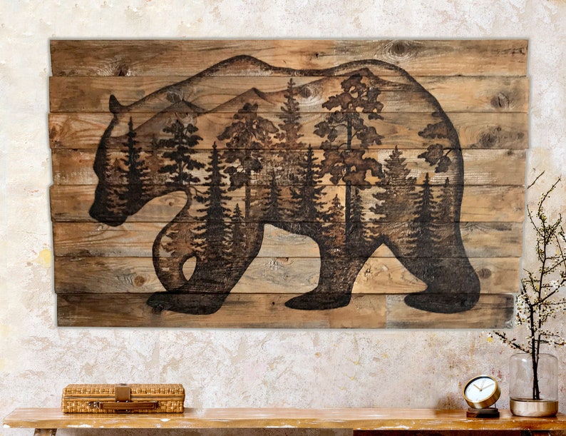 Extra large wall art. Made with reclaimed wood, and features a silhouette of a black bear with a forest scene. Artwork is a wood burning by hand. Wood is a weathered brown. The artwork is dark, burned brown.