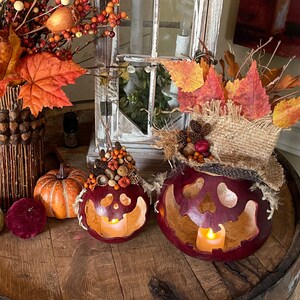 This image shows a fall display of my handmade gourds. They have carved pumpkin faces. They are decorated with fall leaves and berries. The gourds sit on top of a vintage whiskey barrel.