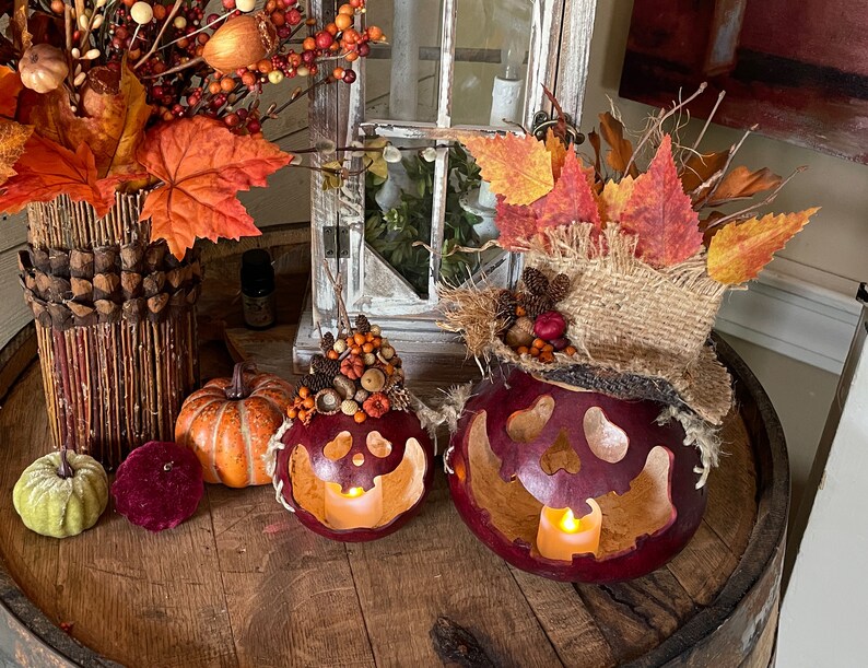 This image shows a fall display of my handmade gourds. They have carved pumpkin faces. They are decorated with fall leaves and berries. The gourds sit on top of a vintage whiskey barrel.