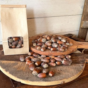 Peut inclure: Nature morte rustique avec des noisettes. Un sac en papier kraft avec une fenêtre montre les noix, à côté d'une planche de service en bois et des noisettes éparpillées sur une surface en bois. Les noix sont brunes avec une coque texturée.