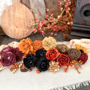 This shows an arrangement with a beige table scarf and autumn colored wood flowers nestle together. Bittersweet berried and a birdhouse sit in the background