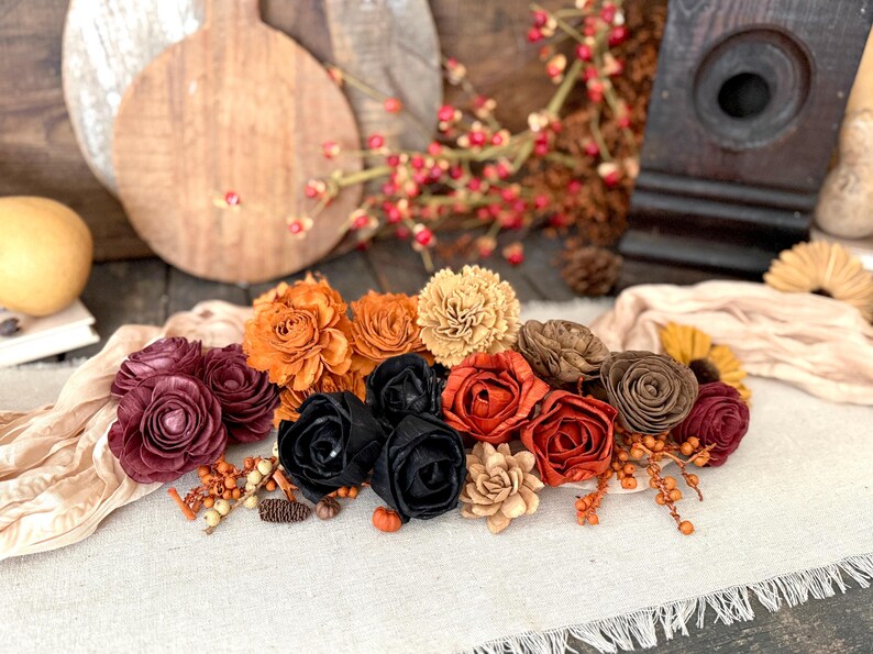 This shows an arrangement with a beige table scarf and autumn colored wood flowers nestle together. Bittersweet berried and a birdhouse sit in the background
