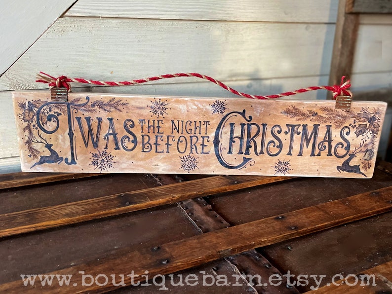 A horizontal wood sign. Twas the night before Christmas and reindeer are wood burned decoratively. The sign hangs with a piece of rope.