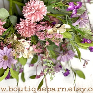 This image shows a close-up of an artificial bouquet of flowers. It features purple daisies, pink mums, and white hydrangeas.