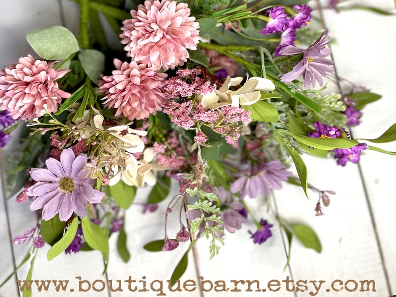 This image shows a close-up of an artificial bouquet of flowers. It features purple daisies, pink mums, and white hydrangeas.