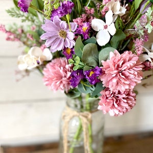 This image shows an artificial bouquet of flowers in a mason jar vase. It features purple daisies, pink mums, and white hydrangeas.