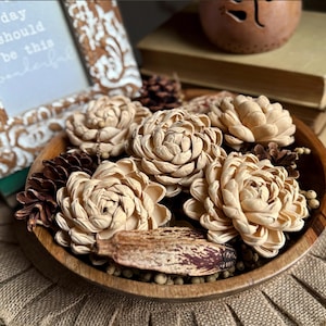 Puede incluir: Un cuenco de madera lleno de flores de madera de sola de color crema. El cuenco está sobre una superficie de arpillera. Las flores están dispuestas en un patrón circular con los tallos hacia adentro. El cuenco está hecho de madera oscura y tiene un acabado natural.