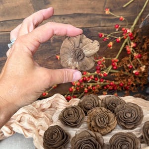 This shows me holding the wood flower blossom so you can see the back view. Several wood flowers are laid out in the background on a decorative table scarf. You can also see bittersweet branches in the back.