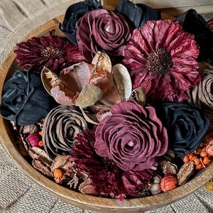This shows a teak wood bowl with a dark wood flower arrangement. The bowl holds dried botanical berries, wood roses, daisies and ranunculus flower blossoms in moody fall colors.