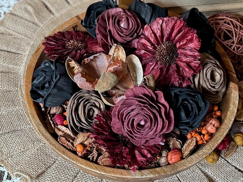 This shows a teak wood bowl with a dark wood flower arrangement. The bowl holds dried botanical berries, wood roses, daisies and ranunculus flower blossoms in moody fall colors.