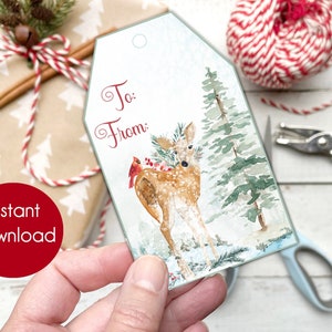 May include: A printable Christmas gift tag featuring a watercolor illustration of a deer in a snowy forest with a cardinal bird. The tag has the words "To:" and "From:" written on it.