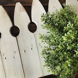 A bouquet of artificial boxwood greenery on a farmhouse fence.