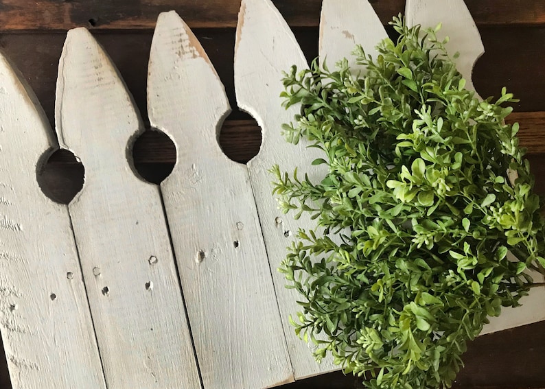 A bouquet of artificial boxwood greenery on a farmhouse fence.