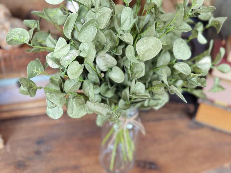 This is atop view of a bouquet of fake eucalyptus greenery. The sprays sit in a glass jar.