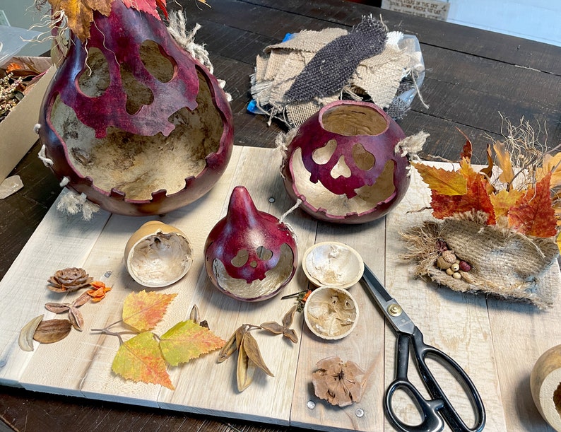 This image shows my workstation where I make the Halloween gourds. The items I use to create the fall gourds are laying on the table. It shows a dried gourd, fall leaves, and scissors laying on the table.