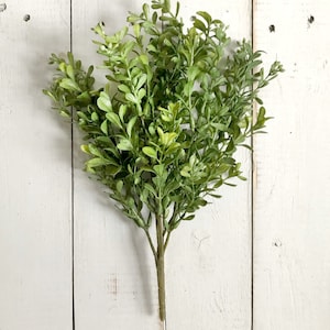 A spray of artificial boxwood greenery on a farmhouse fence.