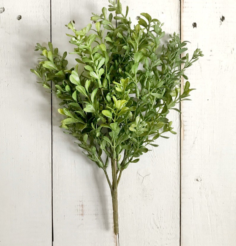 A spray of artificial boxwood greenery on a farmhouse fence.