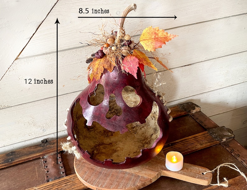 This image shows a large mouth pumpkin gourd decoration. It is a real dried gourd with a carved face. The pumpkin is 12 inches tall and 8.5 inches wide. The gourd is stained berry color. The pumpkin is named Humphrey.