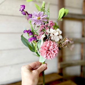 This image shows me holding one faux flower spray. The bundle features a pink mum, a purple daisy, a white hydrangea, and greenery.