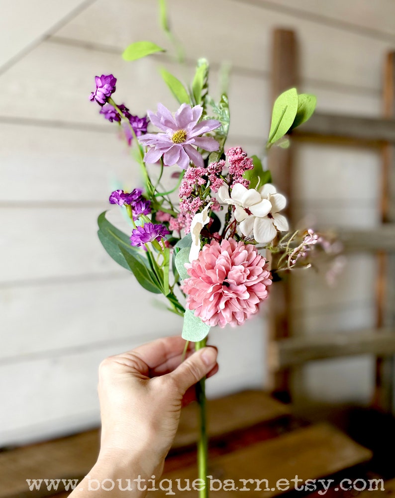 This image shows me holding one faux flower spray. The bundle features a pink mum, a purple daisy, a white hydrangea, and greenery.