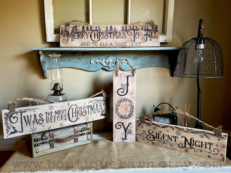 A collection of Christmas signs on reclaimed wood. Signs hang with a piece of rope.