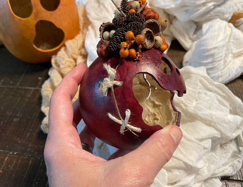 This image shows me holding a fall gourd. I have carved a decorative scare on the side of a little ghost. I stitched the scare up with a hemp cord.