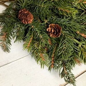A bouquet of artificial Christmas pine sprays on a farmhouse fence.