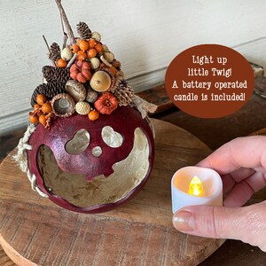 This is a handmade pumpkin decoration. It is a real dried gourd, with a carved ghostly facial expression. The shell has been stained a burgundy color. A battery-operated candle is included.