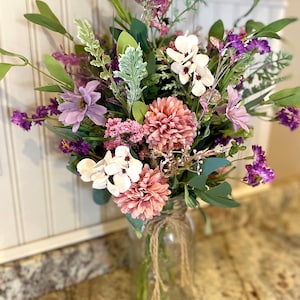 This image shows an artificial bouquet of flowers in a mason jar vase. It features purple daisies, pink mums, and white hydrangeas.