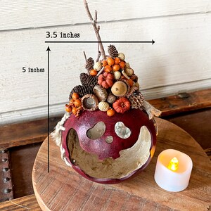 This is a handmade pumpkin decoration. It is a real dried gourd, with a carved ghostly facial expression. The gourd is 5 inches tall and 3.5 inches wide.