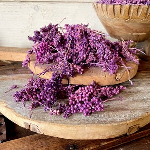 Könnte beinhalten: Getrocknete lilafarbene Blumen, die auf einem Holzbrett angeordnet sind. Die Blumen sind in einer Gruppe angeordnet und haben ein zartes, federleichtes Aussehen.