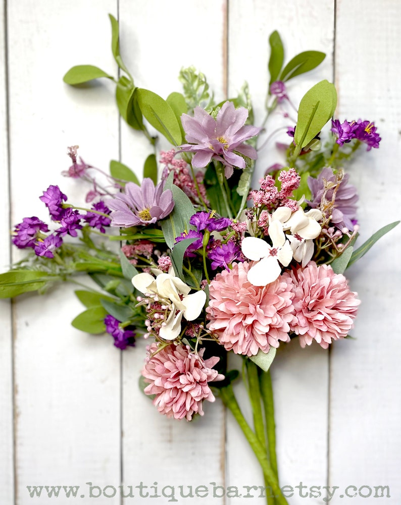 This image shows three faux flower sprays. The bundles feature pink mums, purple daisies, a white hydrangea, and greenery.