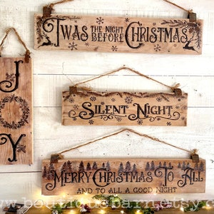 A collection of Christmas signs on reclaimed wood. Signs hang with a piece of rope.