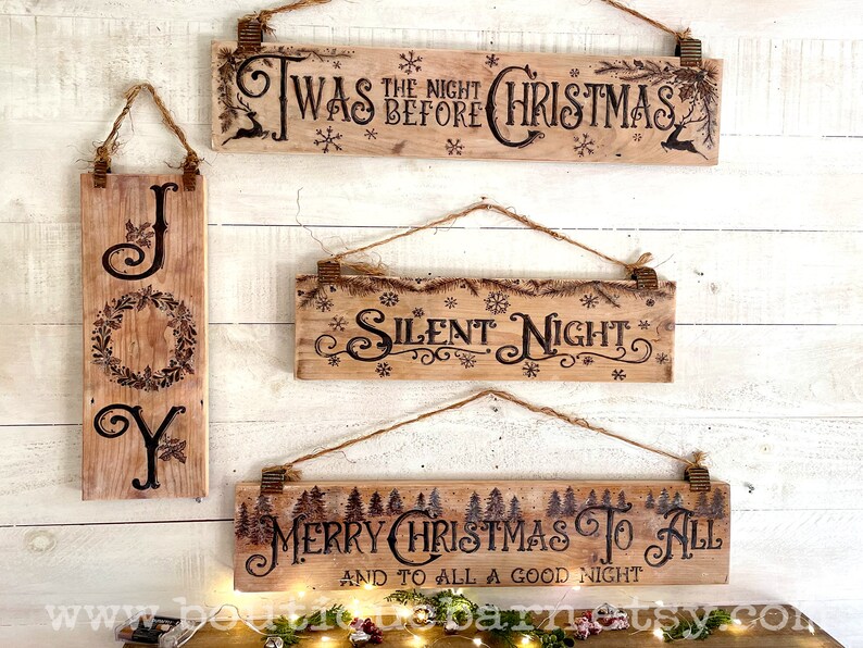 A collection of Christmas signs on reclaimed wood. Signs hang with a piece of rope.