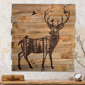 Extra large wall hanging made from reclaimed wood.  It has a dark brown silhouette of a deer with forest scenery inside the body. Birds sit on their antlers. Artwork in wood-burning entirely by hand. The wood is naturally weathered brown.
