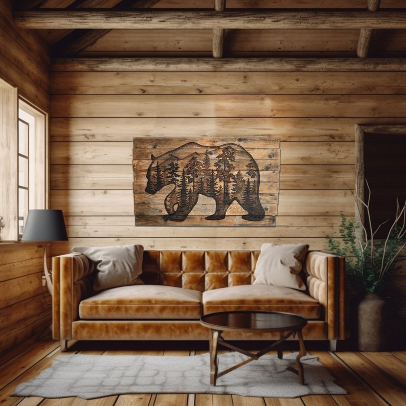 This is a large wood wall hanging featuring a bear and a forest scene. The artwork is wood burned by hand onto a pallet of reclaimed fence. The bear decor is hanging on a log cabin wall over a couch.