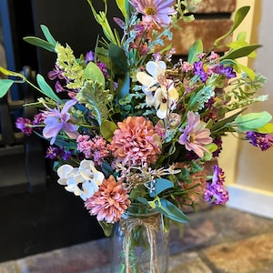 This image shows an artificial bouquet of flowers in a mason jar vase. It features purple daisies, pink mums, and white hydrangeas.