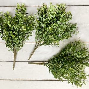 Three sprays of artificial boxwood greenery on a farmhouse fence.