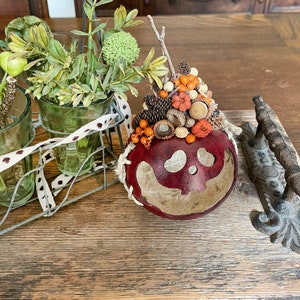 This is a handmade pumpkin decoration. It is a real dried gourd, with a carved ghostly facial expression. The gourd sits on a dinning room table.