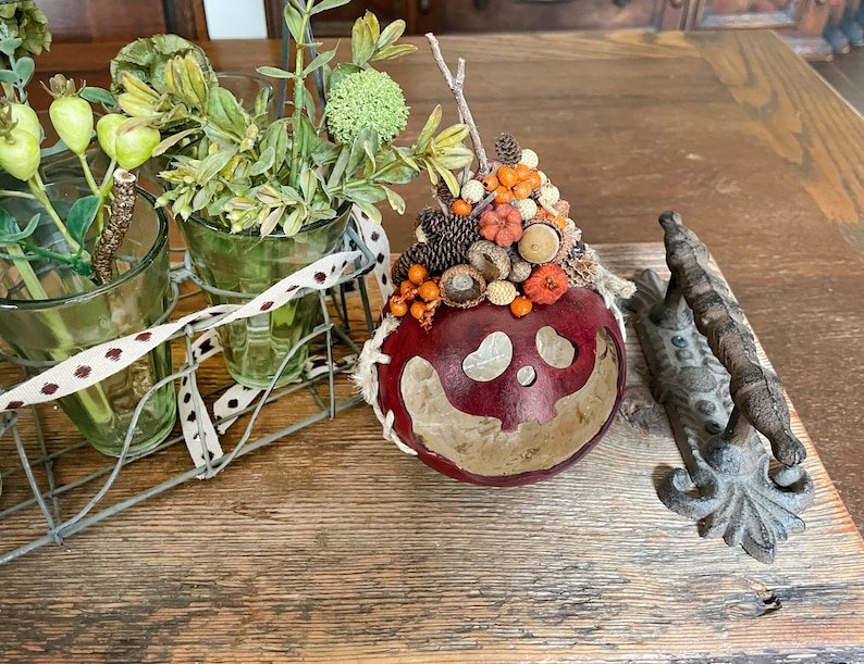 This is a handmade pumpkin decoration. It is a real dried gourd, with a carved ghostly facial expression. The gourd sits on a dinning room table.