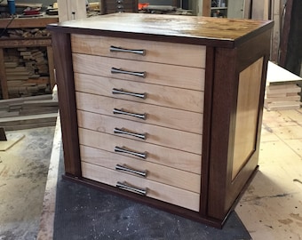 Könnte beinhalten: Ein Holzschrank mit acht Schubladen und einem Nussbaumfurnier. Die Schubladen haben silberne Griffe und sind aus Ahornholz.