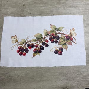 May include: A rectangular piece of white fabric featuring a printed botanical illustration of blackberry branches with dark purple and red berries, green leaves, and two light-colored butterflies positioned on the left and right sides.